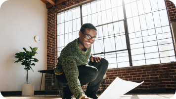 A person smiling and picking a paper from the floor. achive